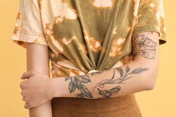 Wall Mural - Young woman with tattooed arm on yellow background, closeup