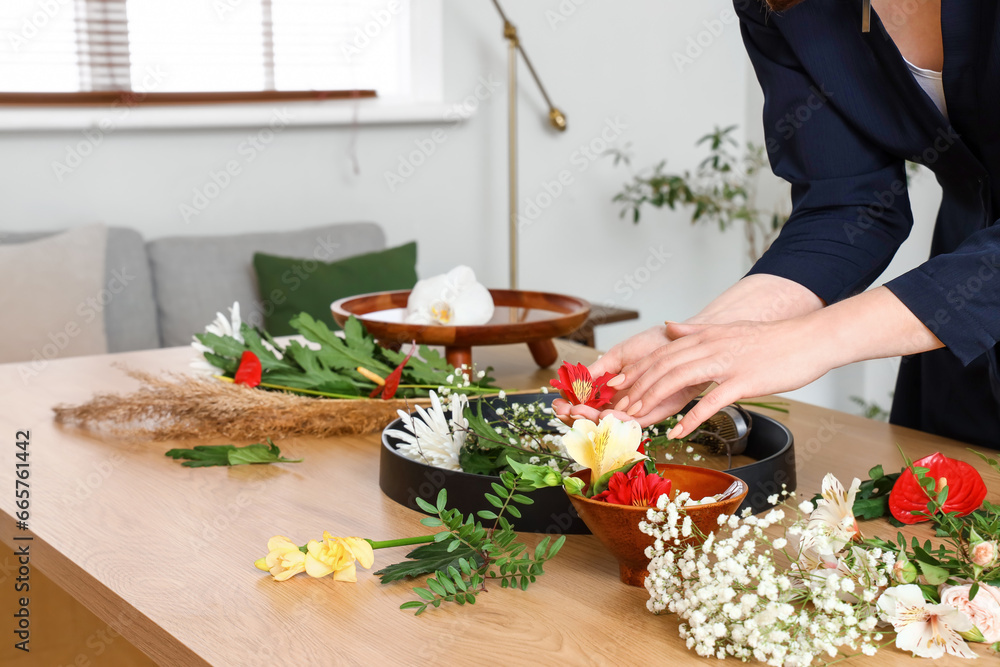 Woman making ikebana at table in room, closeup