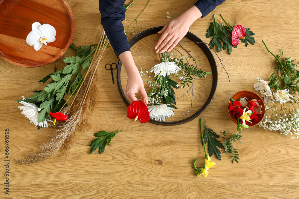 Woman making ikebana on wooden table, top view