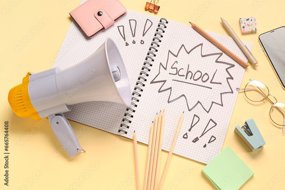 Stationery, megaphone and notebook with word SCHOOL on pale yellow background