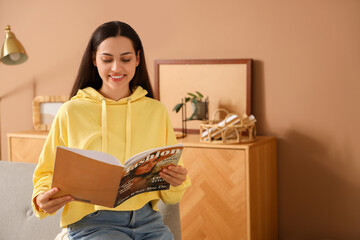 Wall Mural - Young woman in hoodie reading magazine at home