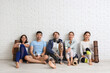 Group of sporty young people with yoga mats sitting near white brick wall