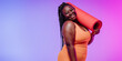 © gstockstudio - Happy plus size African woman in sportswear carrying exercise mat on vibrant background