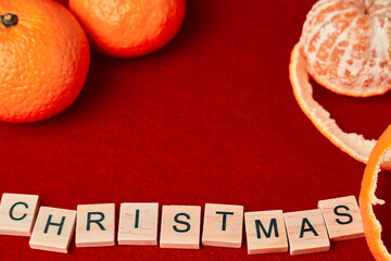 the word christmas composed of wooden letters on a red background with tangerines