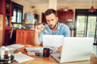 © Geber86 - Concerned young man reading through bank statements at home