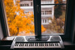 Playing a synthesizer by the window in autumn, with a view of the trees. Melancholy loneliness concept.