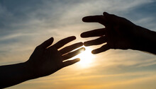 silhouettes of hands reaching out for hope and supporting each other on sunset background