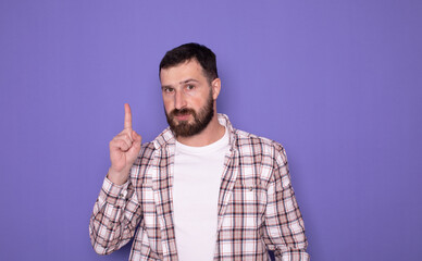 Wall Mural - Young handsome man with beard over purple background. Pointing with finger up and angry expression, showing no gesture. 