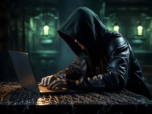 Profile View Of An Individual In A Hooded Sweatshirt And Guy Fawkes Mask Working On A Laptop.