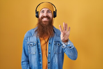 Poster - Caucasian man with long beard listening to music using headphones showing and pointing up with fingers number four while smiling confident and happy.