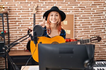 Poster - Young caucasian woman playing classic guitar at music studio smiling with an idea or question pointing finger with happy face, number one