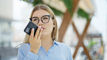 Wall Mural - Young blonde woman business worker sending voice message by smartphone working at street