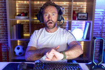 Sticker - Middle age man with beard playing video games wearing headphones in hurry pointing to watch time, impatience, upset and angry for deadline delay