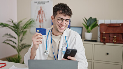 Wall Mural - Young hispanic man doctor using smartphone working doing online shopping at clinic