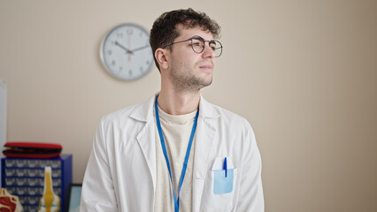 Poster - Young hispanic man doctor standing with serious expression looking to the side at clinic