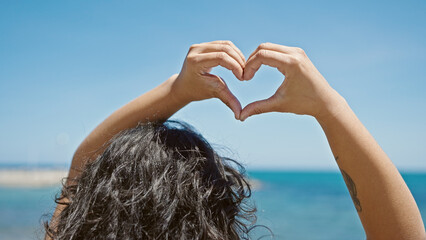 Poster - Young beautiful hispanic woman tourist doing heart gesture standing backwards at beach