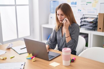 Wall Mural - Young blonde woman business worker using laptop talking on smartphone at office