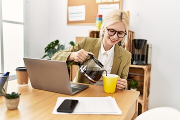 Canvas Print - Young blonde woman business worker using laptop pouring coffee on cup at office