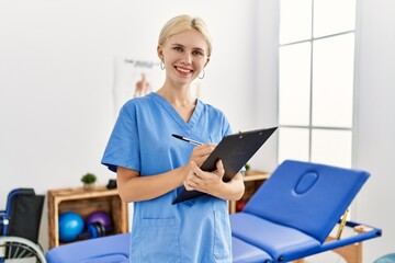 Wall Mural - Young blonde woman pysiotherapist smiling confident writing on document at rehab clinic