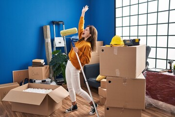 Canvas Print - Young blonde woman singing song using paint roller as a microphone at new home