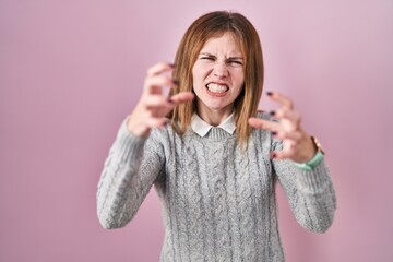 Wall Mural - Beautiful woman standing over pink background shouting frustrated with rage, hands trying to strangle, yelling mad