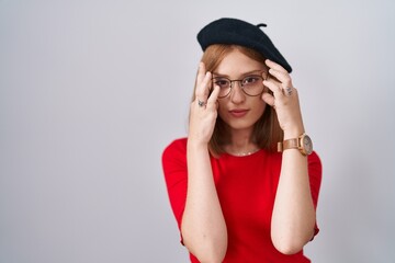 Sticker - Young redhead woman standing wearing glasses and beret trying to open eyes with fingers, sleepy and tired for morning fatigue