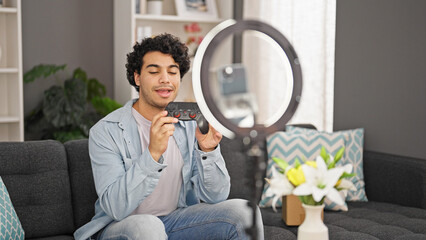 Canvas Print - Young latin man holding joystick recording video tutorial at home