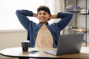 Satisfied arabic guy takes break at workplace in home office