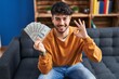 © Krakenimages.com - Hispanic man with beard holding 100 dollars banknotes doing ok sign with fingers, smiling friendly gesturing excellent symbol