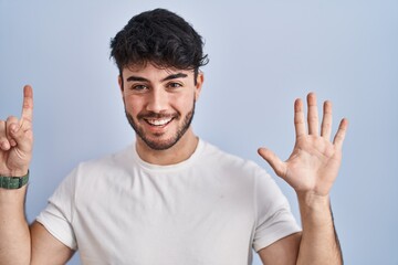 Sticker - Hispanic man with beard standing over white background showing and pointing up with fingers number six while smiling confident and happy.