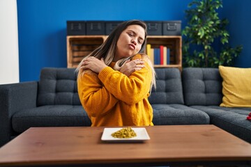 Wall Mural - Young hispanic woman eating green peas hugging oneself happy and positive, smiling confident. self love and self care