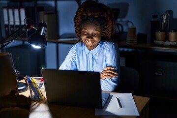 Wall Mural - African woman working at the office at night happy face smiling with crossed arms looking at the camera. positive person.