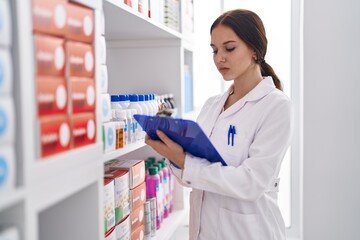 Poster - Young woman pharmacist writing on clipboard at pharmacy