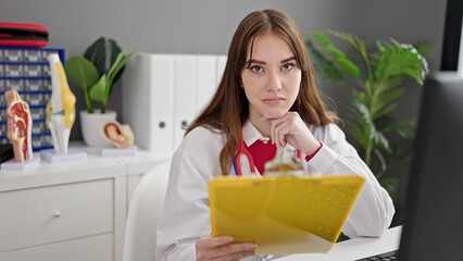 Poster - Young hispanic woman doctor reading medical report with serious expression at clinic