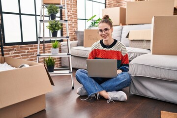 Poster - Young hispanic girl sitting on the floor at new home with laptop looking positive and happy standing and smiling with a confident smile showing teeth