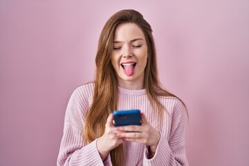 Canvas Print - Young caucasian woman using smartphone typing message sticking tongue out happy with funny expression.