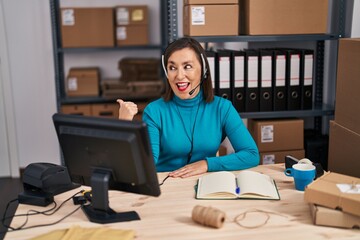 Poster - Middle age hispanic woman working at small business ecommerce on customer support pointing thumb up to the side smiling happy with open mouth