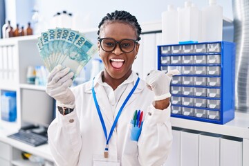 Sticker - African woman with braids working at scientist laboratory holding money pointing thumb up to the side smiling happy with open mouth