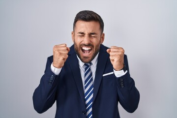 Wall Mural - Handsome hispanic man wearing suit and tie excited for success with arms raised and eyes closed celebrating victory smiling. winner concept.