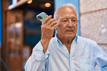 Canvas Print - Senior grey-haired man listening audio message by the smartphone at street