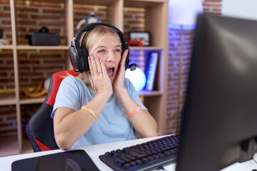 Canvas Print - Young caucasian woman playing video games wearing headphones afraid and shocked, surprise and amazed expression with hands on face