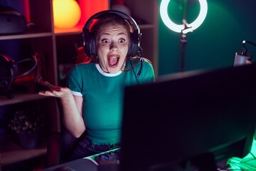 Wall Mural - Redhead woman playing video games celebrating mad and crazy for success with arms raised and closed eyes screaming excited. winner concept