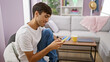 © Krakenimages.com - Radiant young hispanic man sitting at home, having a blast texting on his smartphone, a picture of happier times. his glowing smile sets a cheerful atmosphere. enjoying the indoor coziness.