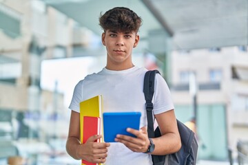 Poster - Young hispanic teenager student using touchpad holding books at university