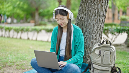 Sticker - Young chinese woman using laptop and headphones sitting on floor at park