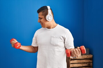 Poster - Young latin man listening to music using dumbbells training at sport center