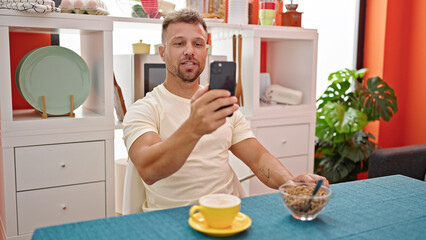 Canvas Print - Young man having breakfast doing video call at dinning room