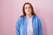 Young hispanic woman with red hair standing over pink background looking sleepy and tired, exhausted for fatigue and hangover, lazy eyes in the morning.