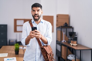 Poster - Hispanic man with beard using smartphone at the office angry and mad screaming frustrated and furious, shouting with anger looking up.