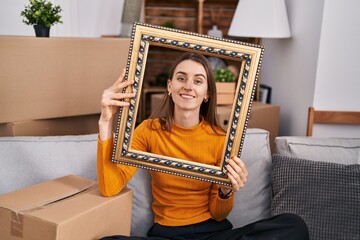 Poster - Young caucasian woman at new home holding empty frame smiling with a happy and cool smile on face. showing teeth.